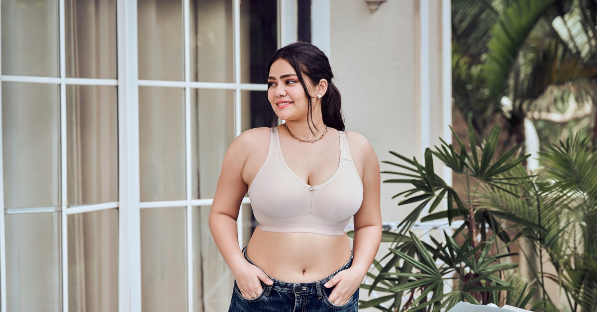 A curvy woman in a nude full-coverage bra by a window